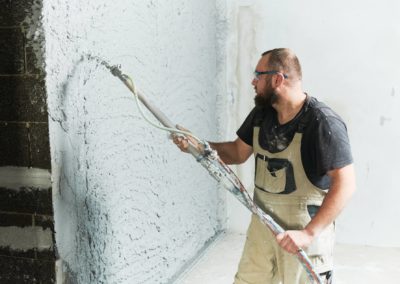 Plasterer using screeder spraying putty plaster mortar on wall