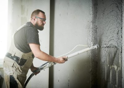 Plasterer using screeder spraying putty plaster mortar on wall